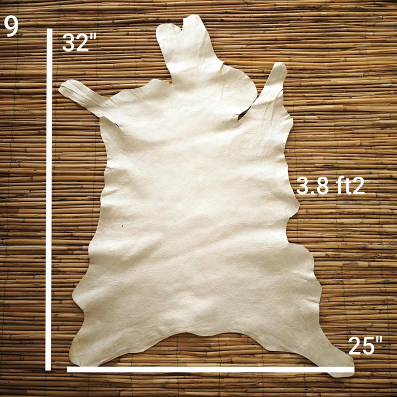 May include: Off-white leather hide, approximately 32 inches by 25 inches, with a surface area of 3.8 square feet. The hide has an irregular shape and is displayed against a bamboo background. The image shows the dimensions of the hide.