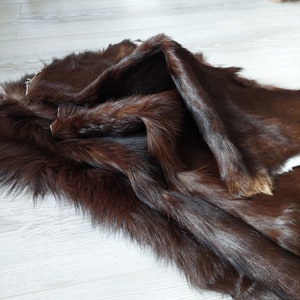 May include: A brown fur pelt with long, soft fur. The fur is folded in half, showing the underside of the pelt.