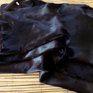 Può includere: Primo piano di una pelle scura, possibilmente nera. La pelle è piegata e ha una consistenza lucida e liscia. L'illuminazione crea riflessi e ombre, enfatizzando la consistenza e il colore del materiale. L'aspetto generale suggerisce un prodotto in pelle di alta qualità.