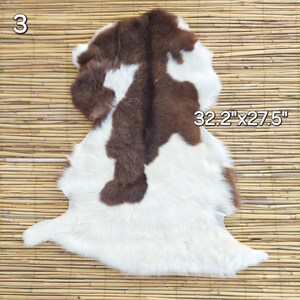May include: A cowhide rug with a brown and white pattern. The rug measures 32.2 inches by 27.5 inches. The number "3" is visible in the upper left corner. The rug is placed on a bamboo mat.