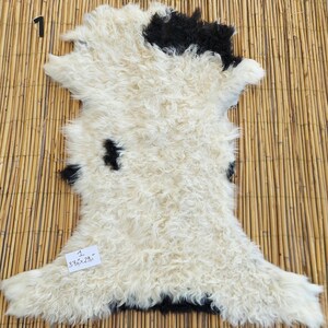 May include: White sheepskin rug with black patches. The rug is approximately 37 inches by 29 inches.
