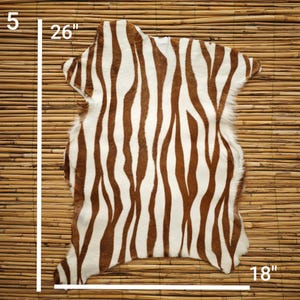 May include: A decorative zebra-print rug with brown and white stripes. The rug measures 26 inches long, 18 inches wide, and 5 inches high. The rug is made of a soft material and is suitable for home decor.
