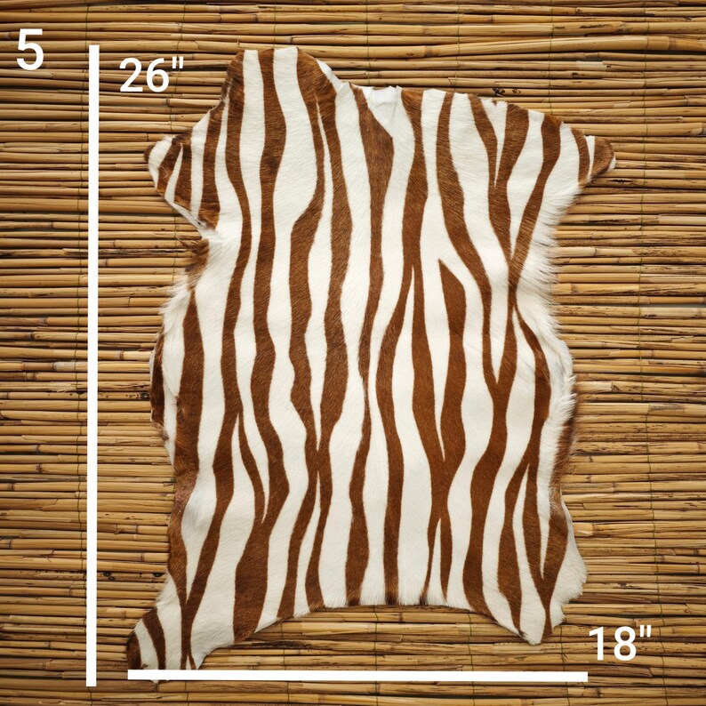 May include: A decorative zebra-print rug with brown and white stripes. The rug measures 26 inches long, 18 inches wide, and 5 inches high. The rug is made of a soft material and is suitable for home decor.
