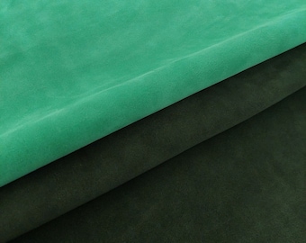 May include: Two pieces of fabric, one a dark green and the other a bright teal green, are folded over each other. The fabric has a soft, suede-like texture.