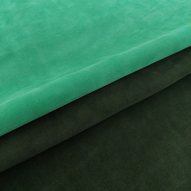 May include: Two pieces of fabric, one a dark green and the other a bright teal green, are folded over each other. The fabric has a soft, suede-like texture.