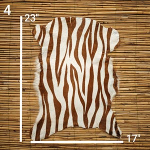 May include: A zebra-striped rug with brown and white patterns. The rug measures 23 inches long and 17 inches wide, with a 4-inch edge. The rug is made of a soft material and is suitable for home decor.