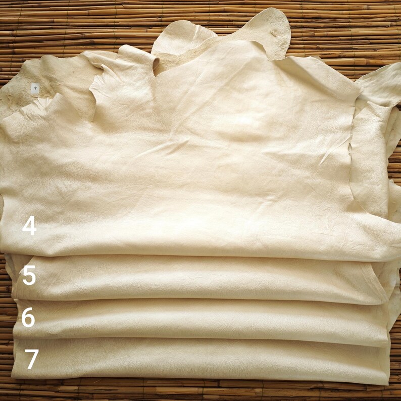 May include: A stack of cream-colored leather hides, with visible textures and folds. The edges of the hides are uneven, and the numbers 4, 5, 6, and 7 are visible on the side. The hides are stacked on a bamboo mat.