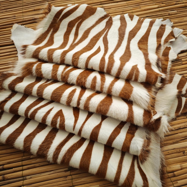 May include: A stack of zebra-striped hides with brown and white patterns. The hides are arranged in a layered fashion, showcasing the natural texture and color variations. The hides are on a bamboo surface.