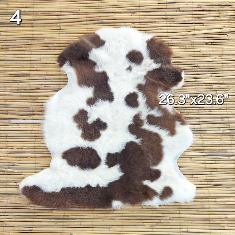 May include: A cowhide rug with a brown and white spotted pattern. The rug measures 26.3 x 23.6 inches. The rug is placed on a bamboo mat.