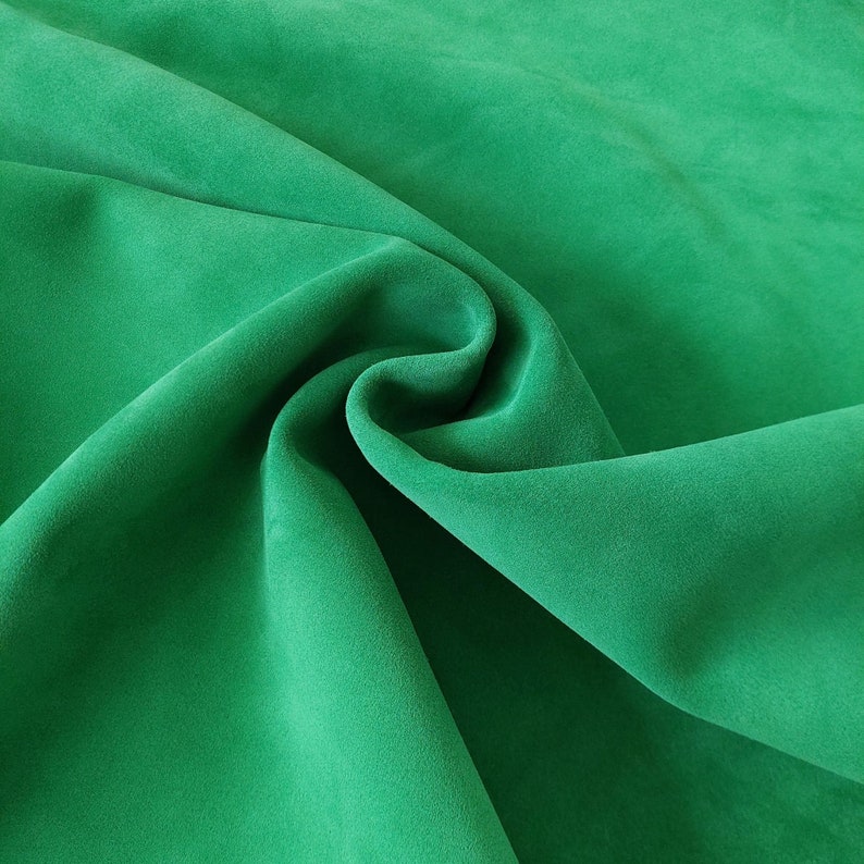 May include: A close-up of a soft, green fabric with a smooth texture. The fabric is folded and draped, creating a flowing, elegant look.