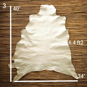 May include: A cream-colored leather hide, approximately 40 inches by 34 inches, with a surface area of 6.4 square feet. The hide has irregular edges and a natural texture. The background is a woven bamboo mat.