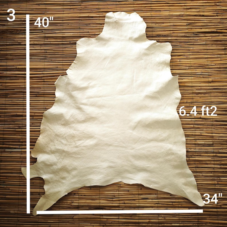 May include: A cream-colored leather hide, approximately 40 inches by 34 inches, with a surface area of 6.4 square feet. The hide has irregular edges and a natural texture. The background is a woven bamboo mat.