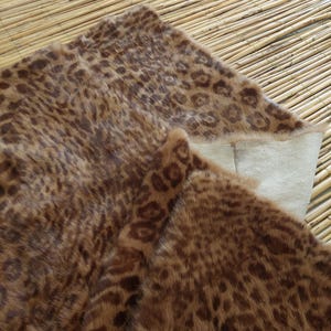 May include: A brown and tan faux fur rug with a leopard print pattern. The rug is folded over, revealing a cream-colored backing. The rug is placed on a bamboo mat.