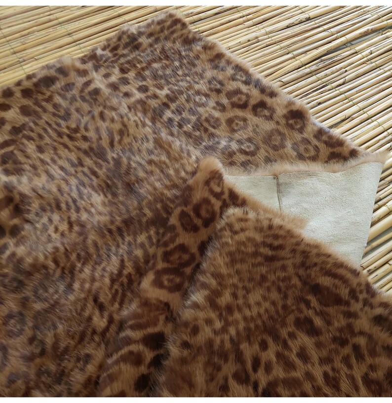 May include: A brown and tan faux fur rug with a leopard print pattern. The rug is folded over, revealing a cream-colored backing. The rug is placed on a bamboo mat.