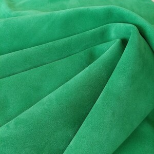 May include: A close-up of a soft, green fabric with a smooth texture. The fabric is folded in a way that creates a series of folds and creases.
