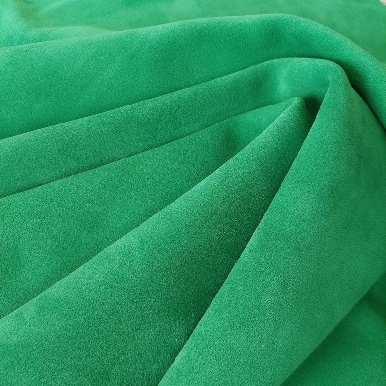 May include: A close-up of a soft, green fabric with a smooth texture. The fabric is folded in a way that creates a series of folds and creases.