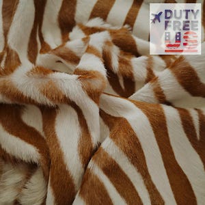May include: Close-up of a textured fabric with a zebra stripe pattern. The fabric features alternating stripes of white and brown. The image includes the text "DUTY FREE US".