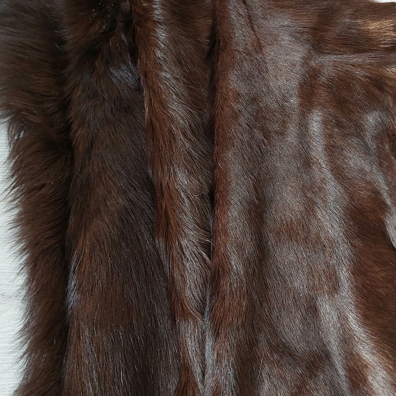May include: Close-up of a brown fur fabric with a soft, plush texture. The fur is arranged in a series of vertical lines, creating a striped pattern.