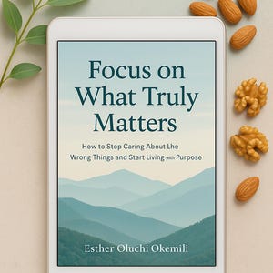 Könnte beinhalten: Ein digitales Tablet zeigt das Buchcover "Focus on What Truly Matters" von Esther Oluchi Okemili. Das Cover zeigt eine ruhige Landschaft mit geschichteten blauen Bergen. Mandeln, Walnüsse und ein Zweig Blätter sind um das Tablet angeordnet.