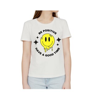 Könnte beinhalten: Weißes T-Shirt mit einer schwarzen und gelben Grafik eines schmelzenden Smiley-Gesichts und dem Text "BE POSITIVE HAVE A GOOD TIME".