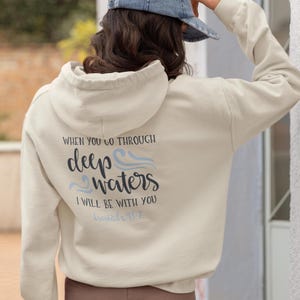 May include: A cream-coloured hoodie with a blue and white graphic that says "When you go through deep waters I will be with you Isaiah 43:2".