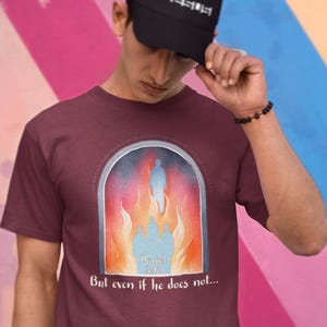May include: A maroon t-shirt with a graphic of a person walking through a fiery archway. The graphic includes the text "Daniel 3:18" and the words "But even if he does not..."