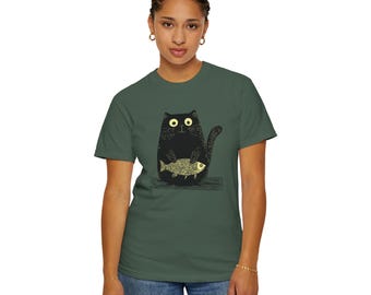 May include: A dark green t-shirt featuring a black cat holding a yellow fish. The cat has large, round eyes and a surprised expression.