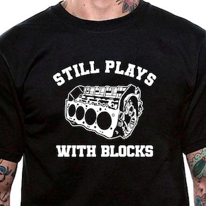 May include: Black t-shirt with a white graphic of an engine and the text "Still Plays With Blocks".