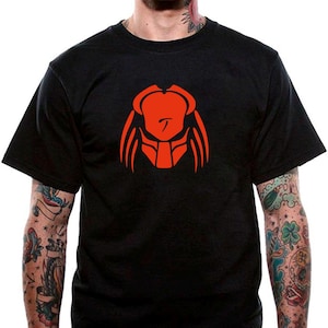 May include: Black t-shirt featuring a red graphic of a Predator mask. The design is centered on the chest. The shirt has short sleeves and a crew neck.