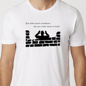 Könnte beinhalten: Ein weißes T-Shirt mit kurzen Ärmeln und einer schwarzen Grafik, die eine Person hinter einer Ziegelmauer zeigt. Der Text lautet: Your father paints roundabouts and your mother shouts at hotels! Das Motiv ist mittig auf der Brust platziert.