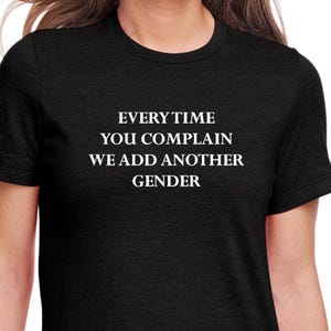 May include: Black t-shirt with white text that reads "EVERY TIME YOU COMPLAIN WE ADD ANOTHER GENDER"