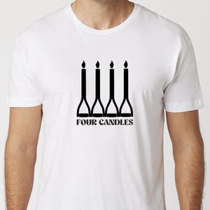 Op de afbeelding: Wit T-shirt met een zwarte afbeelding van vier gestileerde kaarsen met vlammen. De tekst "FOUR CANDLES" staat eronder. Het T-shirt heeft een ronde hals en is gemaakt van zacht materiaal.