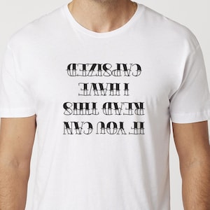 May include: White t-shirt with the text "IF YOU CAN READ THIS I HAVE CAPSIZED" in black, bold, capital letters. The shirt is a crew neck style and appears to be made of a soft material.