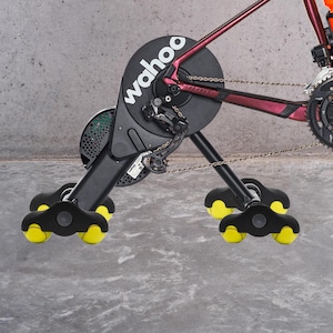 Könnte beinhalten: Ein schwarzer Wahoo-Fahrradtrainer mit gelben Rädern. Der Trainer ist an einem Fahrrad mit einer silbernen Kette befestigt.