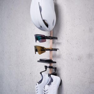 May include: A white bicycle helmet, two pairs of sunglasses, and a pair of white sneakers are hanging on a wooden rack with black metal hooks.