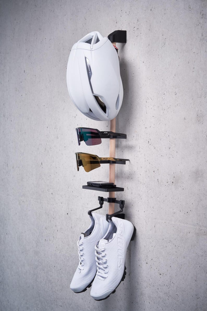 May include: A white bicycle helmet, two pairs of sunglasses, and a pair of white sneakers are hanging on a wooden rack with black metal hooks.