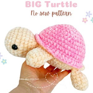 May include: A crocheted turtle in cream and pink. The turtle has a pink shell and cream-colored head, legs, and body. The text "BIG Turtle No sew pattern" is above the turtle. The turtle is held in a hand.