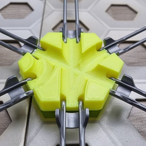 Puede incluir: Una pieza de juego hexagonal amarilla con un diseño en forma de estrella, conectada a seis brazos grises.