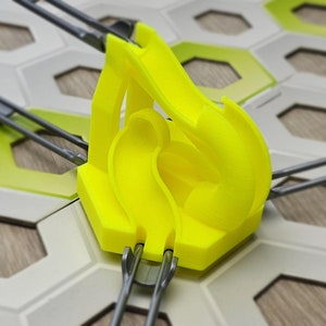 Könnte beinhalten: Ein gelbes Plastik-Spielteil mit einer geschwungenen Bahn für ein Murmelbahn-Spiel. Das Teil ist sechseckig und hat eine graue Metallbahn daran befestigt.