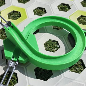 Könnte beinhalten: Eine hellgrüne Spielzeugstrecke aus Kunststoff mit einem Looping-Design. Die Strecke befindet sich auf einer sechseckigen Fliesenbasis mit Kunstraseneinsätzen. Zwei silberne Metallschienen sind an der Strecke befestigt.