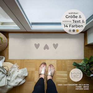 Könnte beinhalten: Beiger rechteckiger Türvorleger mit drei grauen Herzen. Die Matte misst 115 cm x 40 cm. Der Text weist darauf hin, dass sie in 14 Farben und mit oder ohne Text erhältlich ist. Die Matte ist bei 40 Grad maschinenwaschbar.