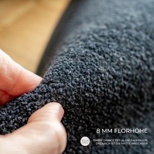 May include: Close-up of a dark gray, textured rug with a pile height of 8 mm. The text on the image states that the color penetrates deep into the fibers, making the rug washable.