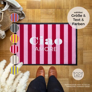 May include: A rectangular doormat with alternating vertical stripes of pink and red. The white text "Ciao AMORE" is centered on the mat. The mat measures 75 cm x 50 cm.