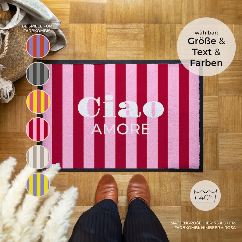 May include: A rectangular doormat with alternating vertical stripes of pink and red. The white text "Ciao AMORE" is centered on the mat. The mat measures 75 cm x 50 cm.