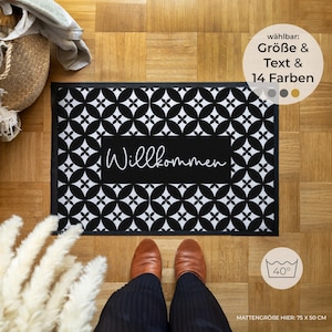 Könnte beinhalten: Rechteckige Willkommensmatte mit einem schwarz-weißen geometrischen Muster und dem Wort "Willkommen" in weißer Schrift. Die Matte misst 75 cm x 50 cm. Das Bild zeigt auch die Füße und Beine einer Person.