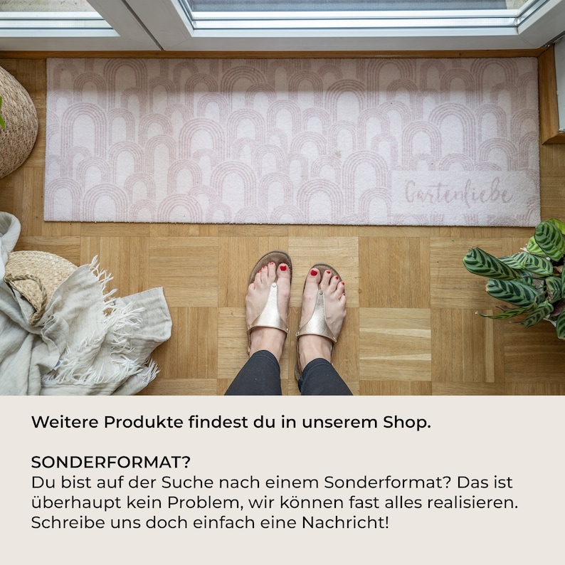 May include: A rectangular, blush-colored doormat with a repeating arch pattern. The text "Gartenliebe" is visible on the mat. The mat is placed on a wooden floor, with a person's feet wearing sandals in the foreground.