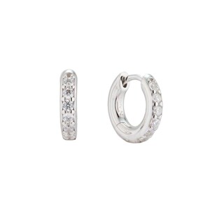 Piccoli cerchietti huggie in argento bagnati in rodio con pietre di zirconia incastonate a griffe. Orecchini NANA impilabili minimalisti sviluppati da Maison Noora