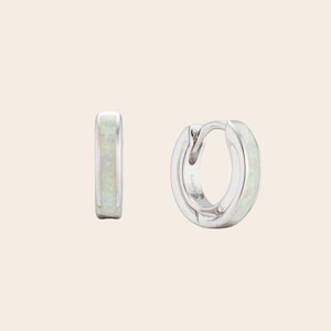 Iridescent white opal inlay huggie hoops. Rhodium-plated dainty silver earrings developed by Maison Noora. Ready-to-gift opal jewelry