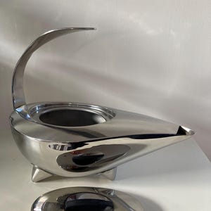 May include: A silver teapot with a unique, modern design. The teapot has a curved spout and a lid that fits snugly on top. The teapot is made of stainless steel and has a polished finish.