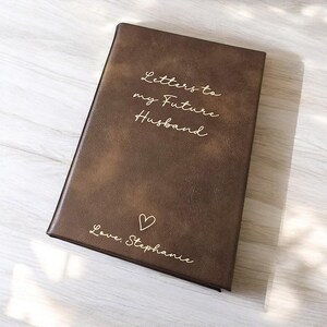 May include: A brown leather-bound journal with the text "Letters to my Future Husband" and "Love, Stephanie" in gold lettering. A small heart symbol is also included.